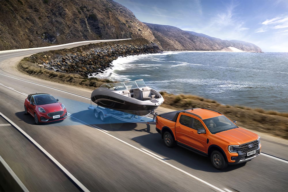 Un Ford Ranger arancione traina una barca lungo un’autostrada costiera, dimostrando la sua capacità di traino.