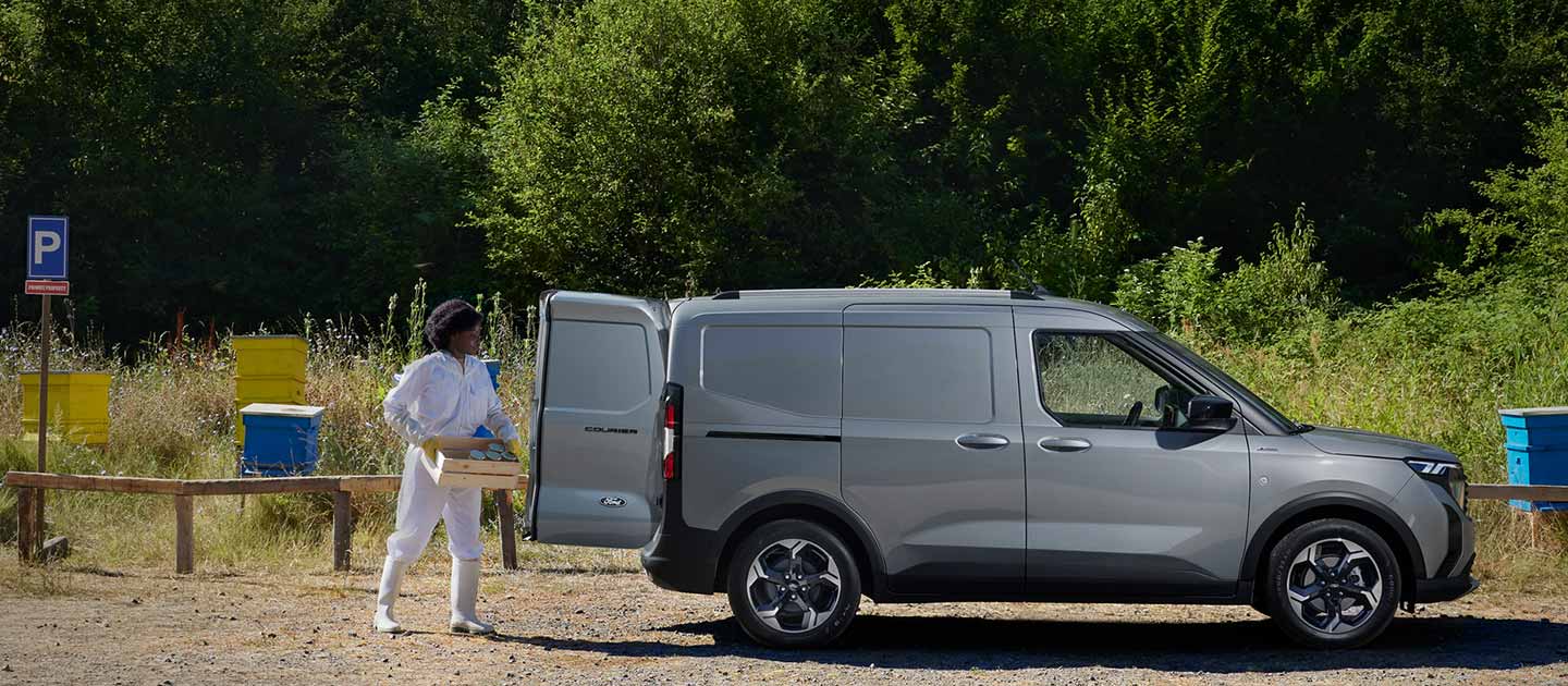 Ford E-Transit Courier grigio – Vista laterale, una donna carica l’auto