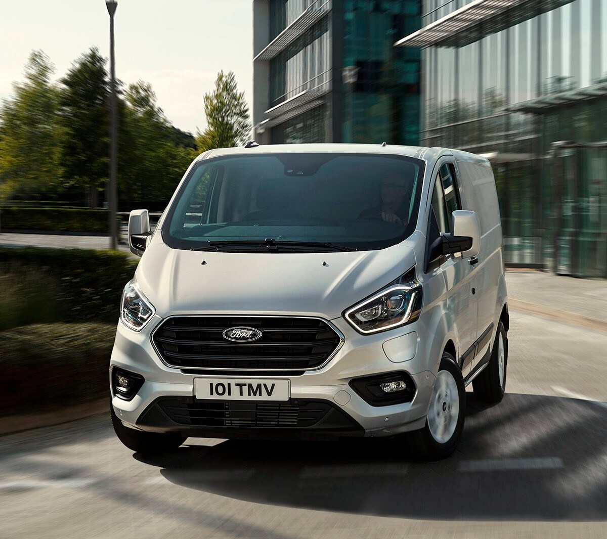 Ford Transit Custom in argento che guida davanti a un edificio con facciata in vetro
