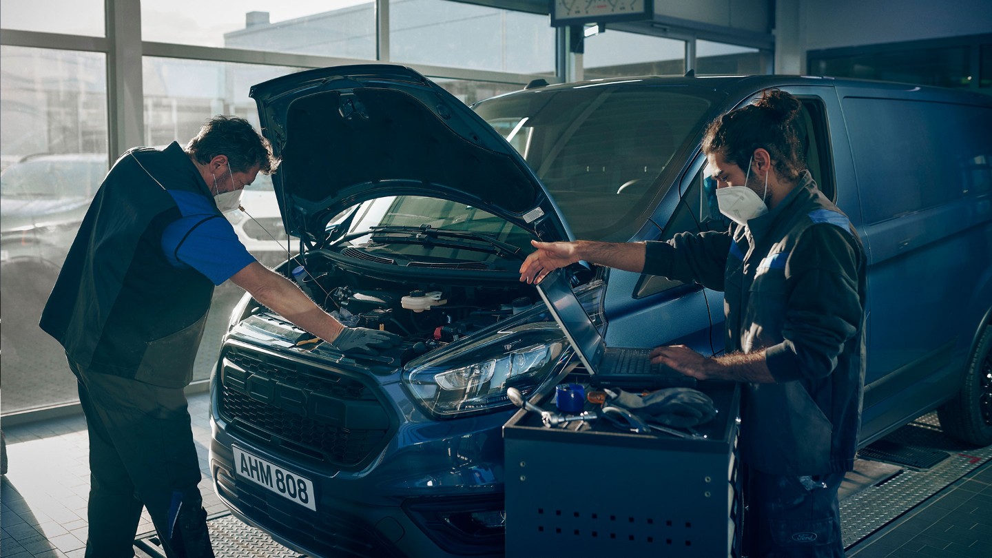 Due meccanici ispezionano un Ford Transit Custom blu con il cofano aperto.