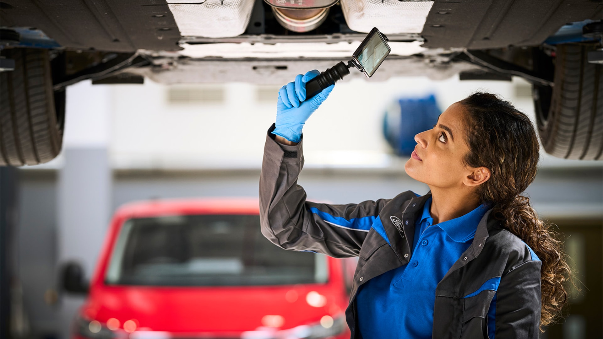 Mechanic inspecting underside of a car with a handheld mirror.