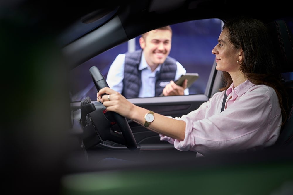 Una donna all'interno di un'auto verde parcheggiata sorride a un concessionario Ford dal finestrino.