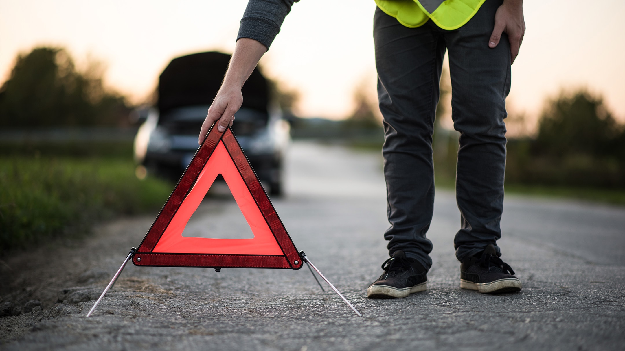 Una persona posiziona un triangolo d’emergenza rosso perché il suo veicolo è in panne a bordo strada.