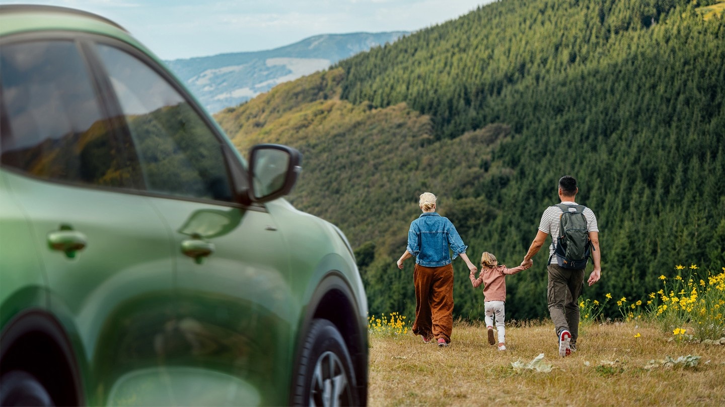 Family walking in a field by a green Ford Kuga