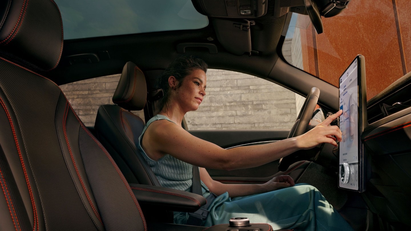 Vista interna. Una donna utilizza dal sedile conducente il touchscreen del SYNC 4A a bordo del suo veicolo