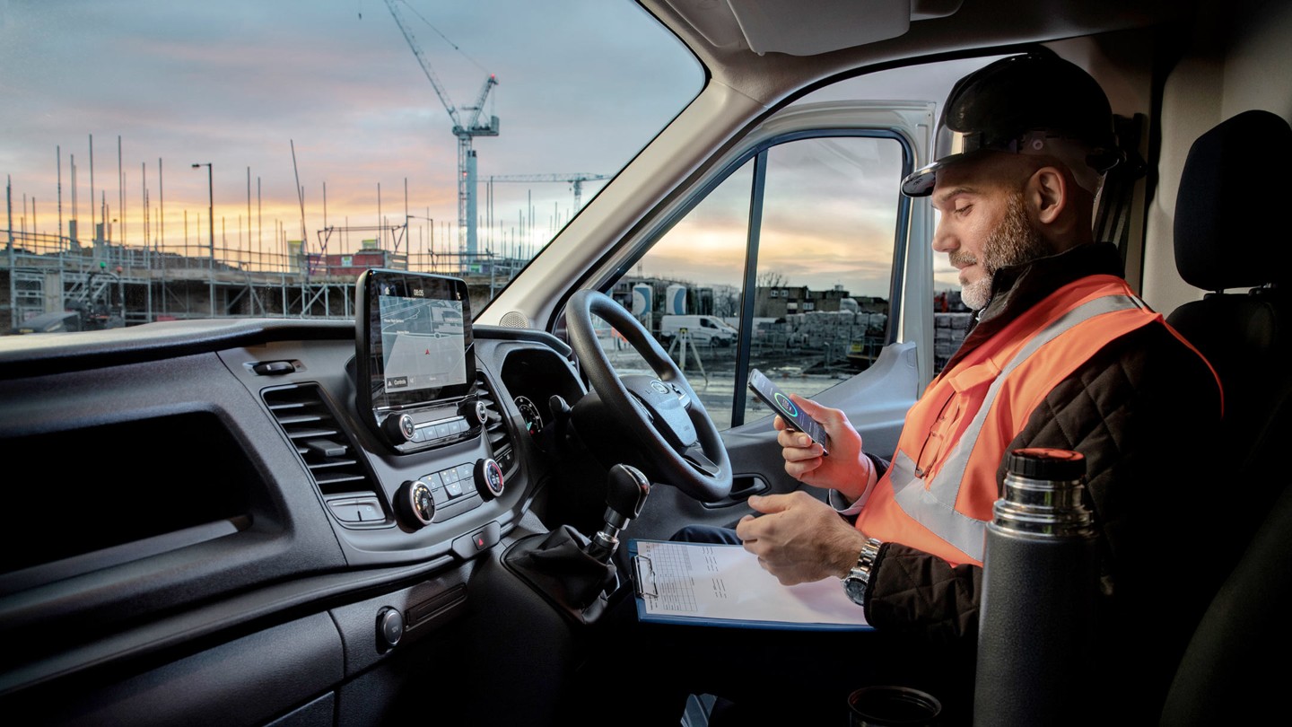 A Ford repairman using his phone while sitting in a Ford Transit